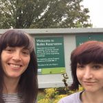 Two smiling women in front of a sign reading "Welcome to the Bullitt Reservation"