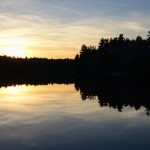 Sunset at the DAR State Forest shows setting sun behind a silhouette of trees, reflected by lake in foreground.