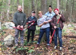 Five college students pose with tools in the woods.