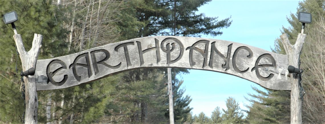 Wooden sign, with the word "Earthdance" carved into it. Trees in the background