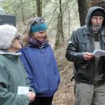 A man reads poetry in the forest while two women listen.