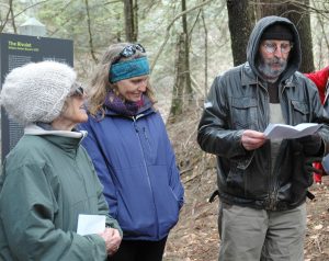 A man reads poetry in the forest while two women listen.