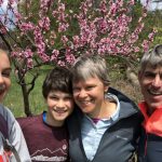 Sally, her husband, and two of her kids in front of a tree with pink blossoms on a recent hike