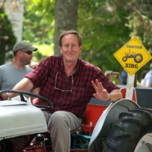 Russell Peotter, sitting in the seat of a tractor and waving to the camera