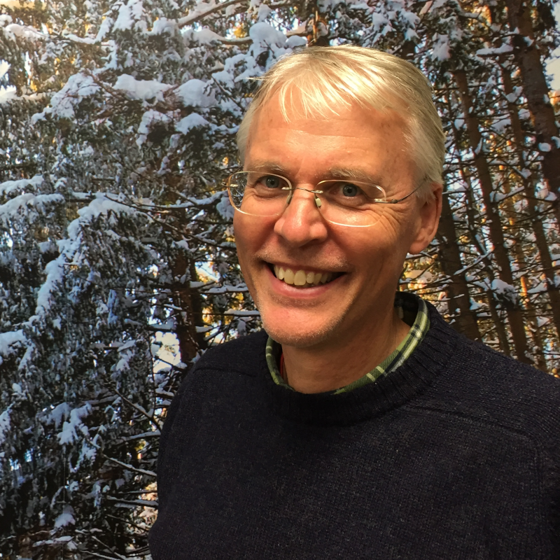 Paul Wetzel, smiling into the camera, standing in front of an image of snow-covered trees