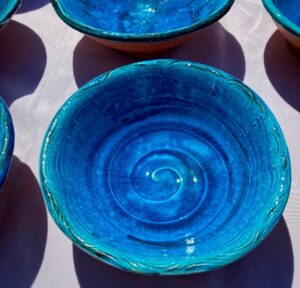 Centered in the image is a vibrant blue ceramic bowl made by Emmett Leader. The edges of other similar bowls can be seen in the image as well.