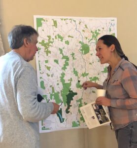 Two standing people talk to each other in front of a large map.