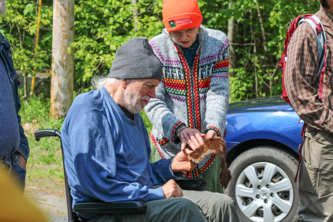 Two people, one standing and one seated in a wheelchair, lean towards each other as they touch and observe a piece of beaver pelt.