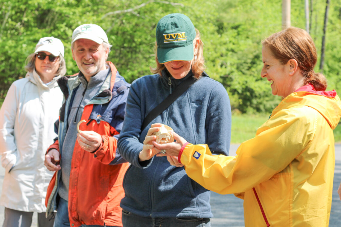 Four standing, smiling people pass a beaver skull and tooth from one person to another.