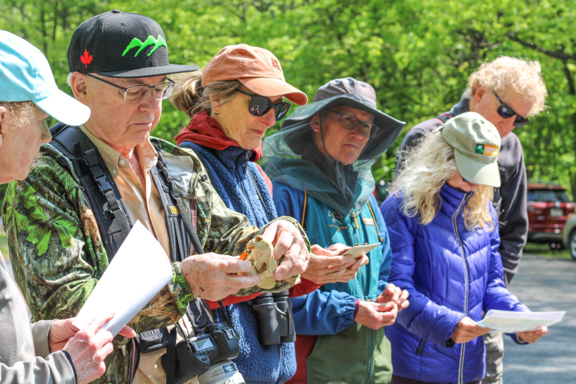 Six standing people observe beaver artifacts, including a skull and diagrams of a beaver lodge.