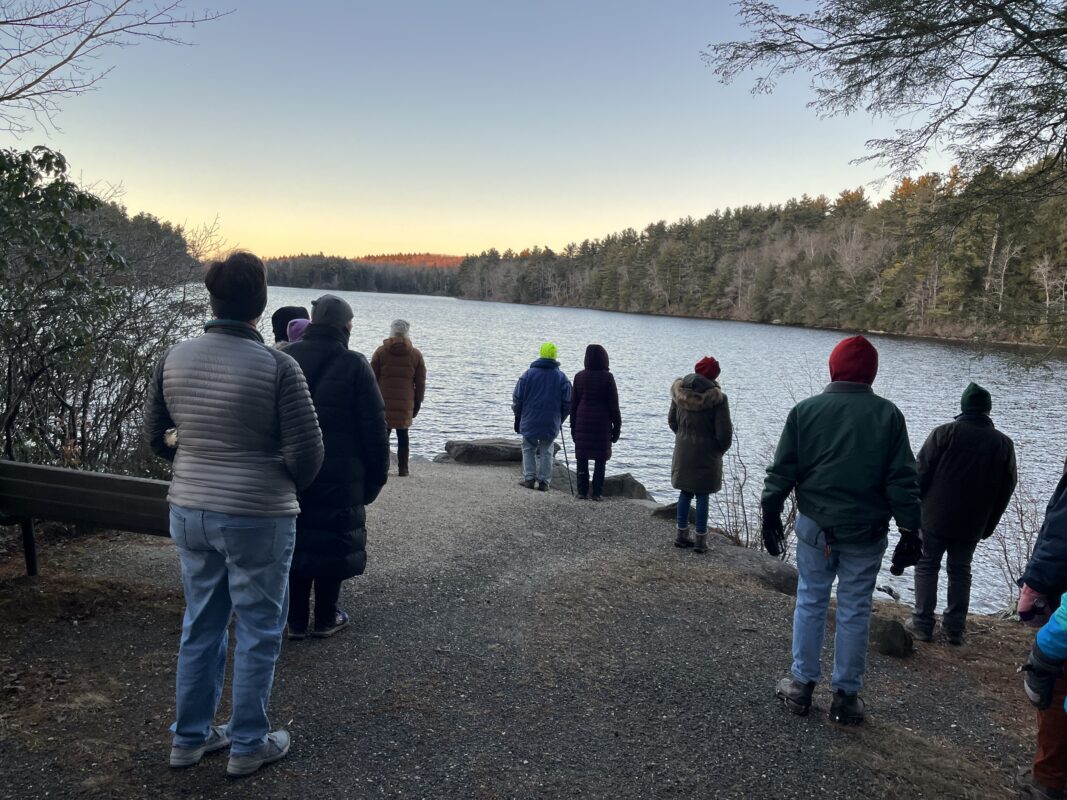 Group of hikers gather together to look over the water, getting a glimpse o first colors of the setting sun.