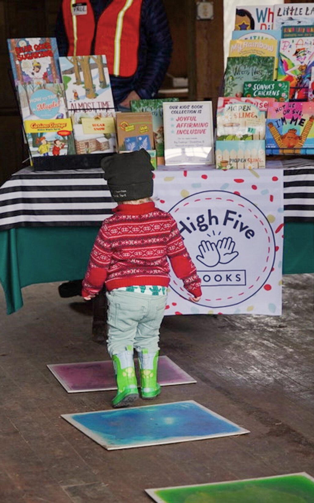 In the barn, child walking towards the High Five Books table of books.