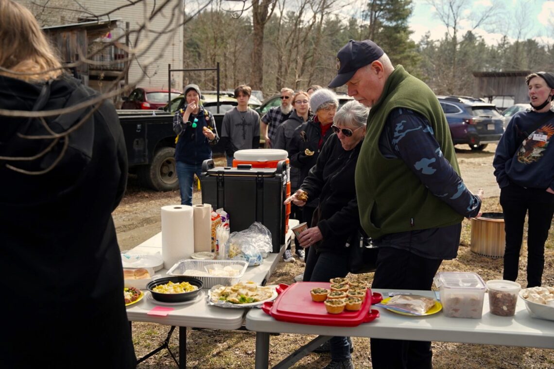 Two people gathered around the community potluck with food out on the table.