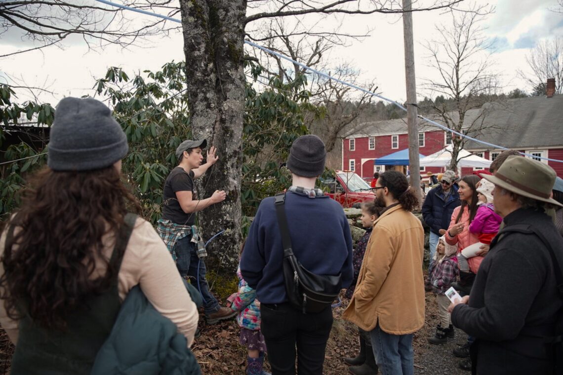 Farmer Pepper giving a tour next to a sugar maple tree with a crowd of people listening around her.