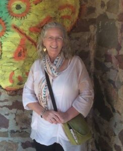 Lori Austin standing in front of a brick wall outside with an abstract painting of a face in multicolor.