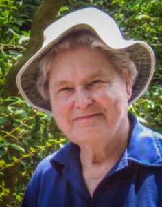 Margaret Waggoner, seen from the shoulders up wearing a blue shirt and a bucket hat, smiles into the camera.