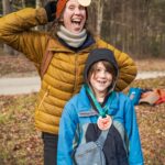 A warmly dressed parent and child smile goofily as they pose with cookie medals.