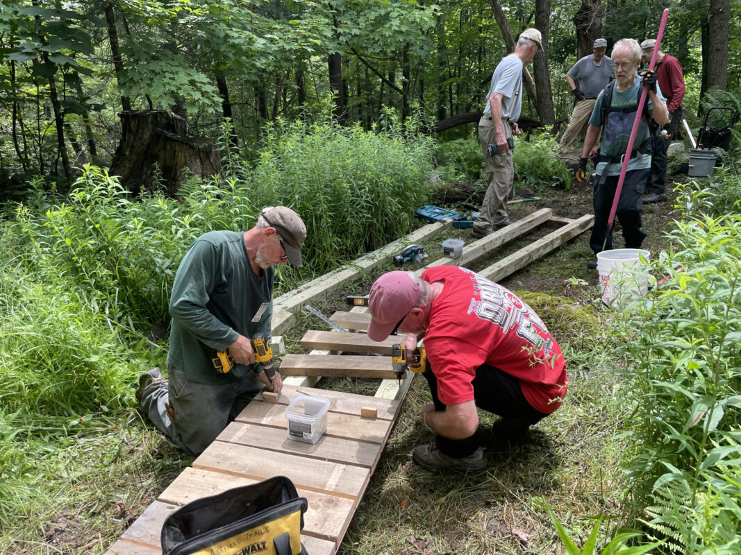 A group of six volunteers screws decking into a wooden boardwalk.